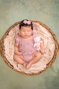 Sleeping newborn baby girl in a pink knitted romper holding a tiny teddy bear, illustrating the successful results of booking a newborn session within the first two weeks with Tender Beginnings Photo.