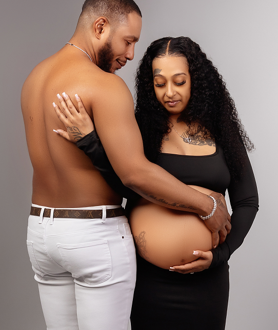 Modern studio maternity portrait of an expecting couple embracing, showing off their unique style with the mother in a fitted black dress.