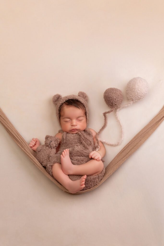 Newborn baby wrapped in a knit bear hat, hammock pose, shot by Tender Beginning