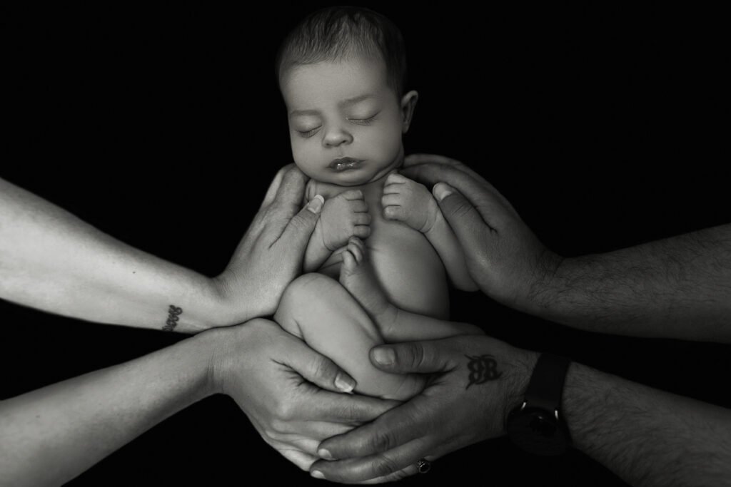 Black-and-white newborn photo held in parents' hands, shot by Tender Beginning