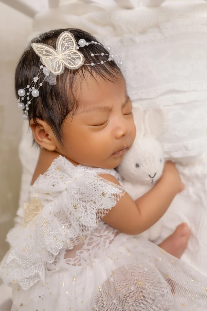 Baby girl sleeping peacefully in a delicate white dress with a plush bunny, showing our flexible styling options.
