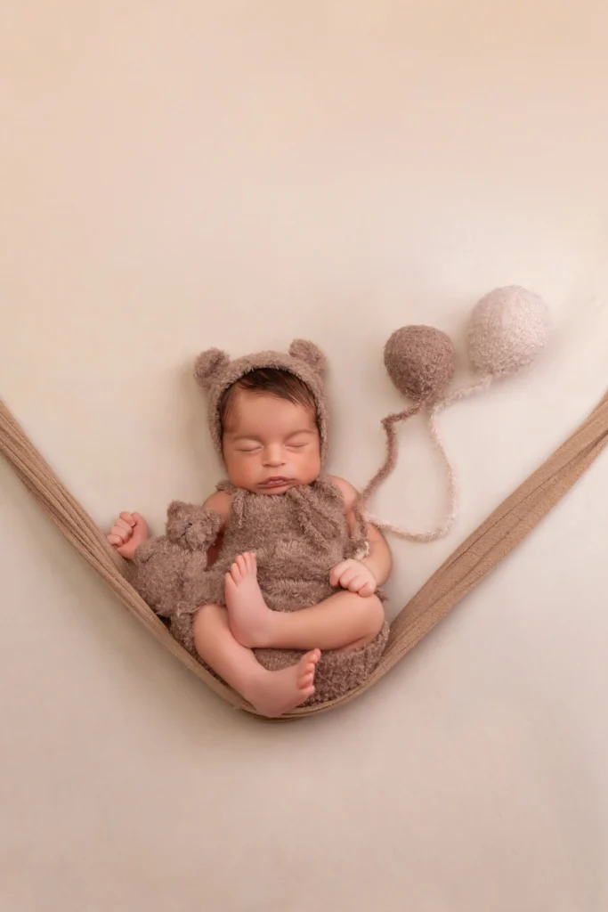 Newborn safely resting in a custom hammock prop wearing a fuzzy brown bear outfit at our Richboro studio.
