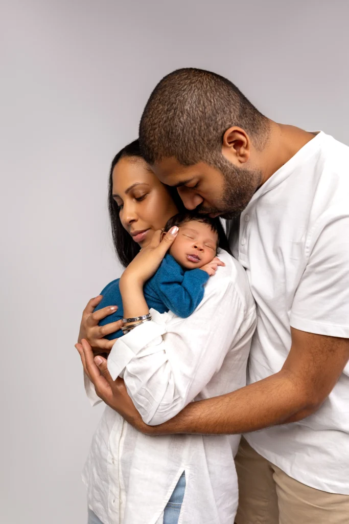 Mother and father sharing a gentle hug while holding their newborn baby in a bright blue outfit, focusing on real family connection during our studio session.
