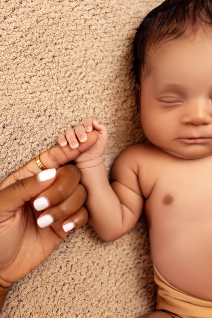 Close-up of a sleeping newborn baby's tiny hand holding onto their mother's finger, capturing a real, unposed connection.