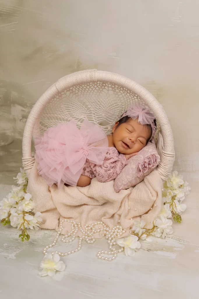 Smiling newborn girl in a bright pink tutu sleeping in a white basket, proving we happily embrace vibrant colors.