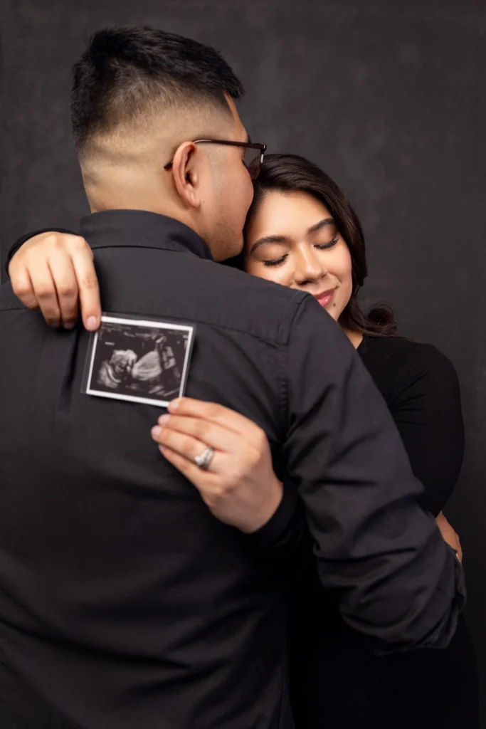 Expecting couple sharing an intimate hug while holding their baby's ultrasound picture during a Philadelphia studio session.