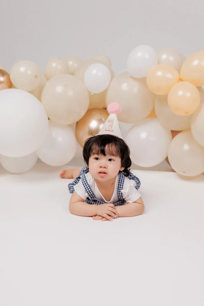 Curious one-year-old boy resting on his tummy in casual denim overalls, capturing natural milestone portraits without stiff poses.