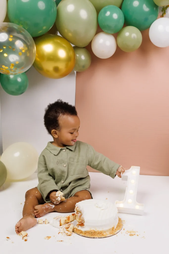 One-year-old boy sitting on the floor tasting his birthday cake beside a marquee one, enjoying an unhurried, child-led cake smash.