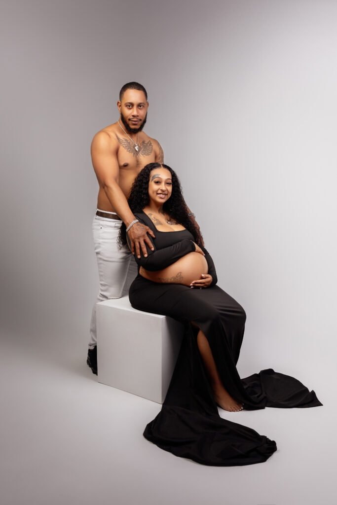 Maternity couple portrait, husband standing behind seated wife, shot by Tender Beginning