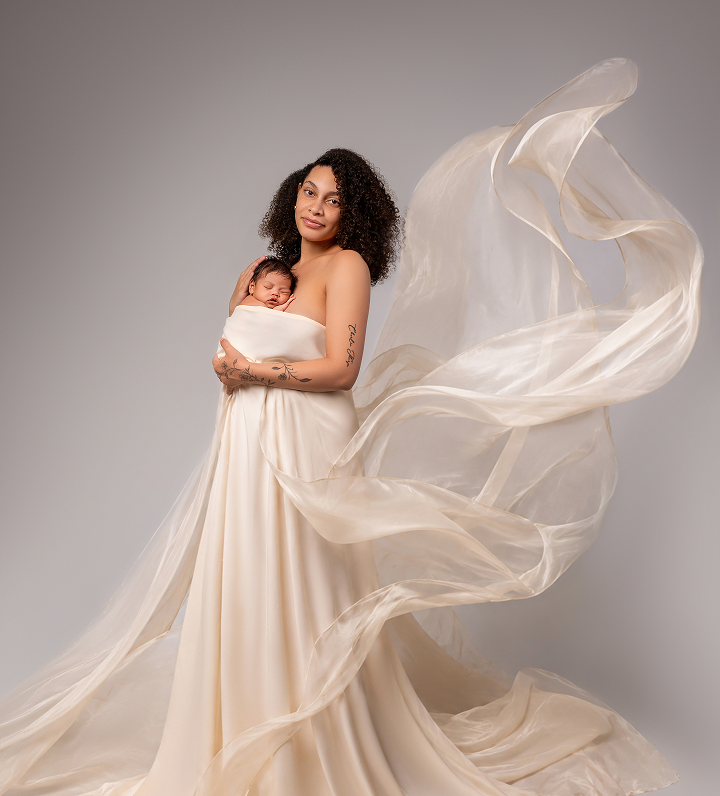 Mother holding her sleeping newborn close while draped in flowing cream silk fabric during a fine art studio session in the Philadelphia area.