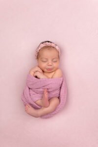 Sleeping newborn baby girl in a pink wrap cradling a knitted bunny toy in a wicker basket, demonstrating the results of a perfectly timed session booked during the second trimester with Tender Beginnings Photo.