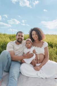 Professional outdoor family portrait in a sun-drenched field, capturing a growing family during a maternity session, showcasing the signature light and airy style of Tender Beginnings.