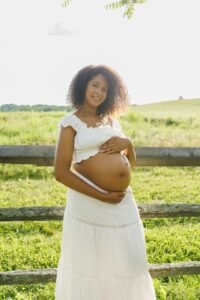 Glowing pregnant woman in a white bohemian dress during an outdoor maternity session at sunset, captured by Tender Beginnings Photo.