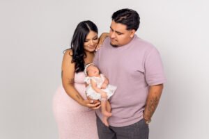 Parents lovingly holding their newborn baby girl during a professional studio family session at Tender Beginnings Photo, featuring coordinated pink and mauve outfits.