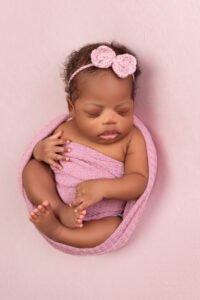 Sleeping newborn baby girl in a pink wrap with a matching crochet flower headband, showcasing the delicate handmade accessories provided by Tender Beginnings Photo studio.